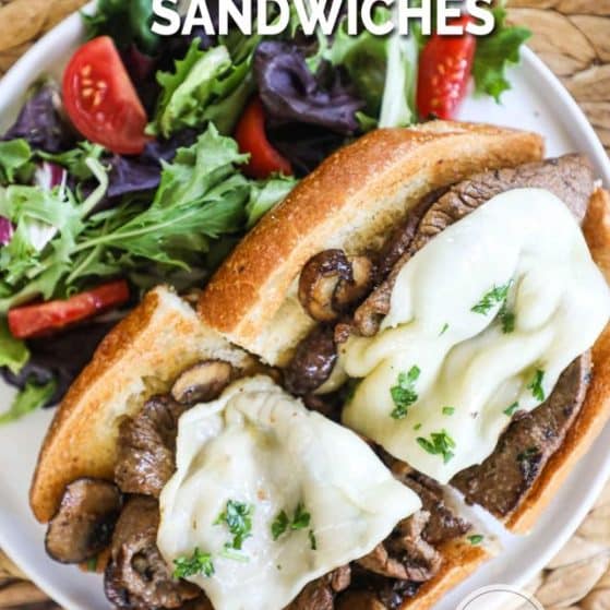 Steak and mushroom sandwich with melted cheese on toasted bread next to a side salad.