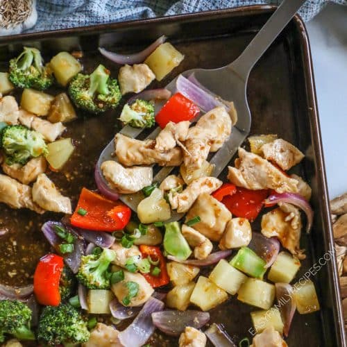 a spatula scooping chicken and veggies from a sheet pan.