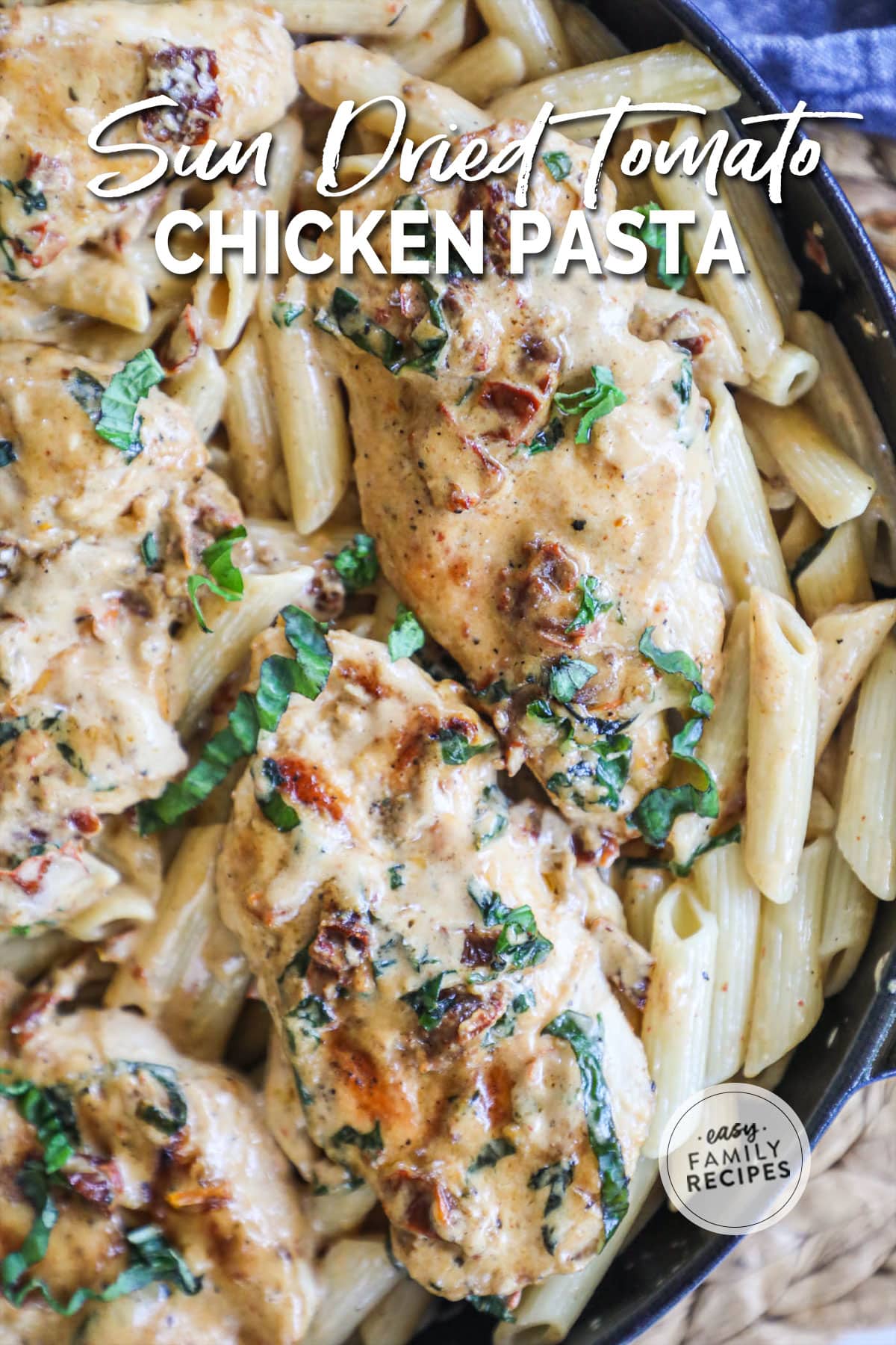 Pasta dish in a skillet with chicken on top and sun dried tomato and basil cream sauce.