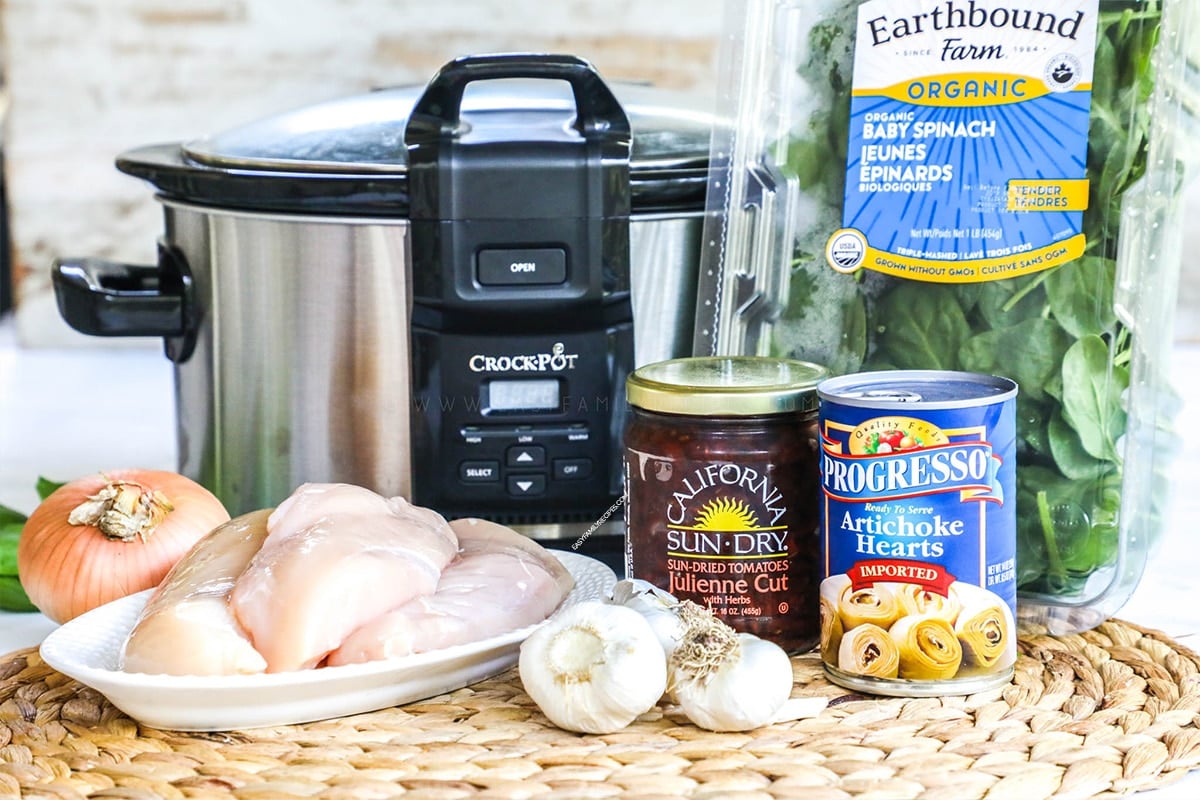 Ingredients for making tuscan chicken in the slow cooker including chicken breast, artichokes, sun dried tomatoes, spinach, garlic, and seasonings.