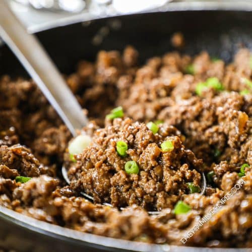 a serving spoon scooping korean beef with green onions on top.