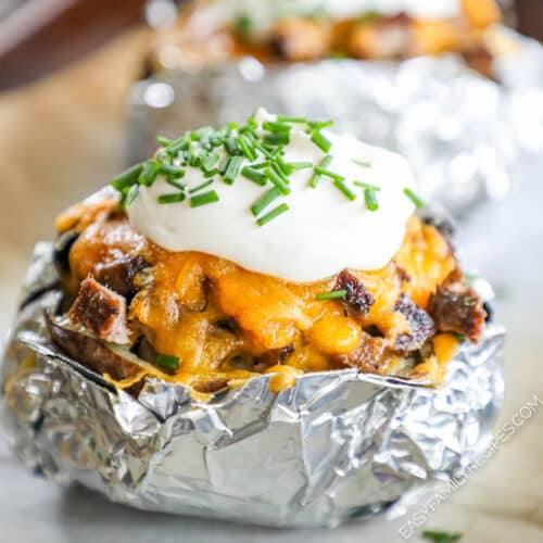 Close up of a baked potato in foil stuffed with chopped steak, cheese, sour cream, and chives.