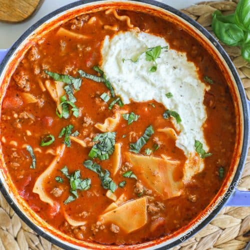 a pot full of lasagna soup with noodles, basil, and ricotta on top.