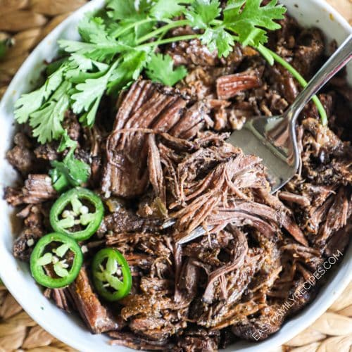 shredded beef barbacoa in a bowl with cilantro and jalapeno slices.