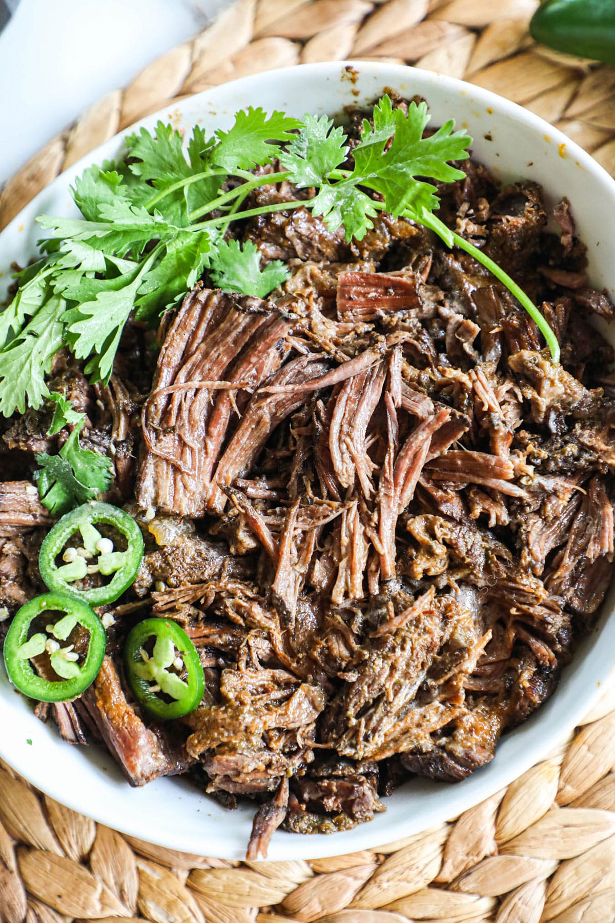 shredded beef barbacoa in a bowl with cilantro and jalapeno slices.