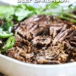 shredded beef barbacoa in a bowl with cilantro and jalapeno slices.
