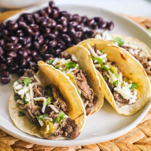 Beef barbacoa tacos on a plate next to black beans.