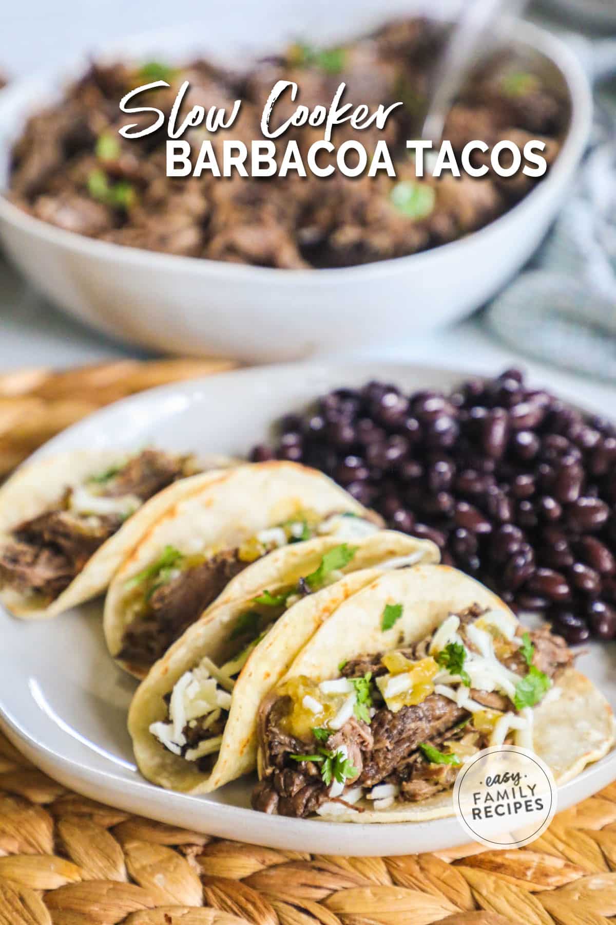 Beef barbacoa tacos on a plate next to black beans with a pan of barbacoa in the back.