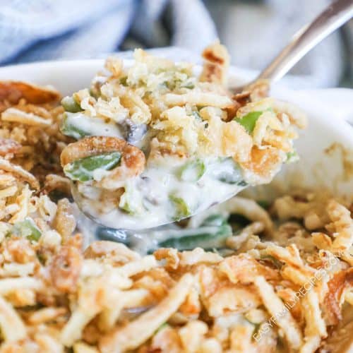 onion topped creamy green bean casserole being spooned out of a casserole dish.