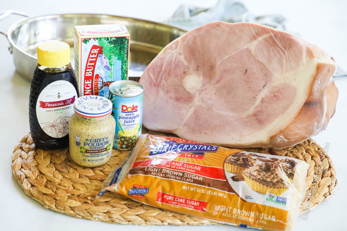 ingredients to make honey glazed ham including a whole ham, butter, Dijon, brown sugar, and pineapple juice.