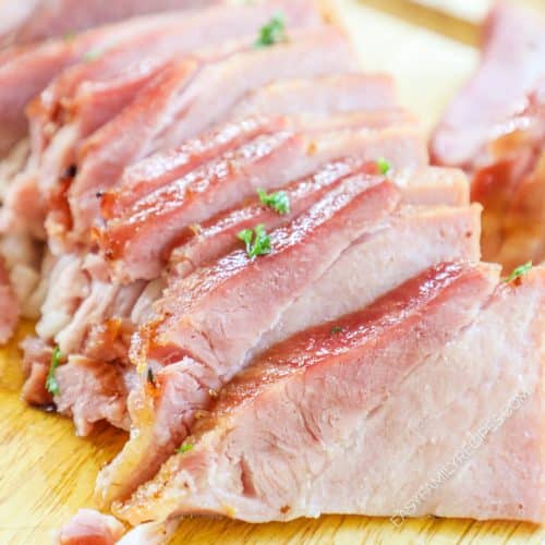 slices of baked glazed ham on a wooden surface cutting board.
