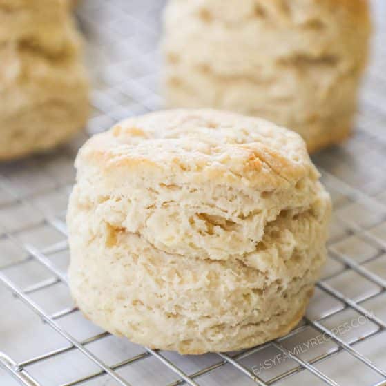 Close up of buttermilk biscuit on wire rack with other biscuits nearby to show height, layers, and biscuit texture.