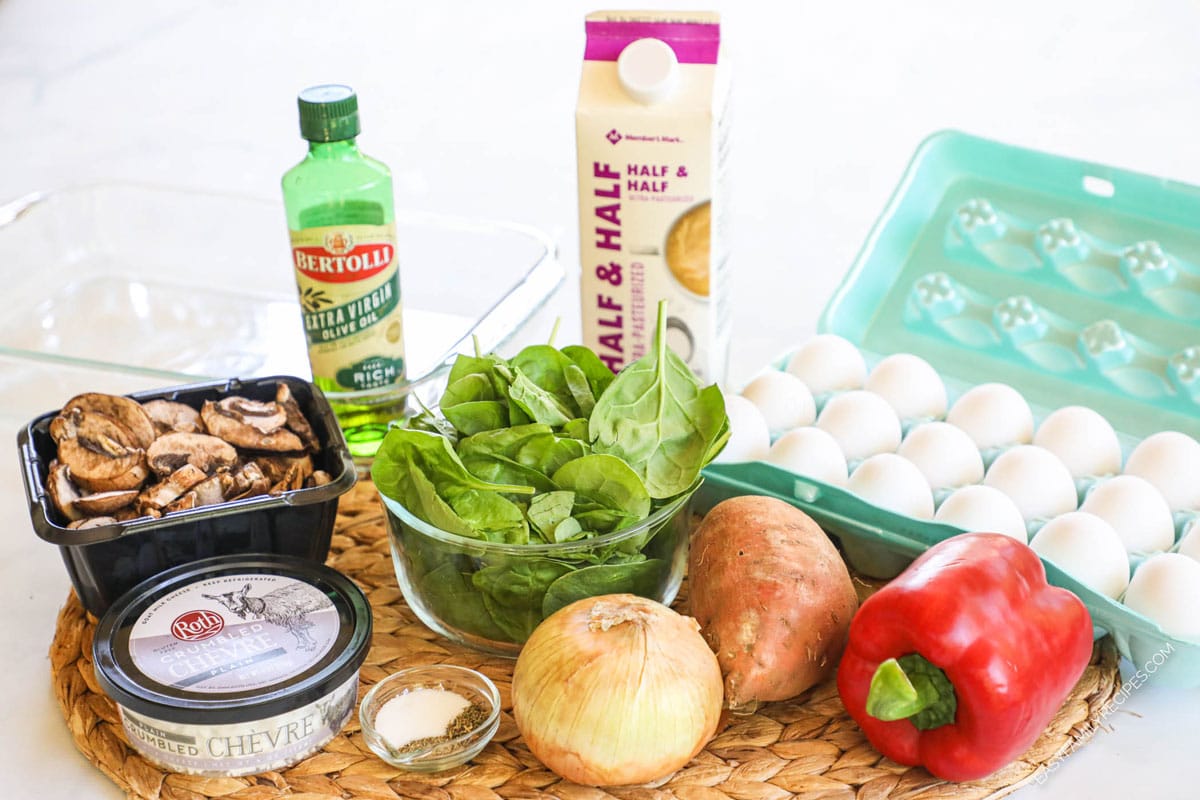 Ingredients to make the casserole including eggs, half and half, olive oil, spinach, sweet potatoes, onion, bell pepper, seasonings, and goat cheese.