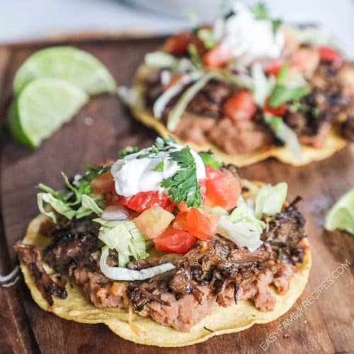 a cutting board filled with barbacoa tostadas and slices of lime.