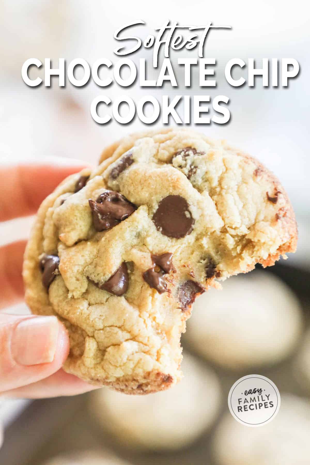 Close up of a hand holding a soft chocolate chip cookie with a bite taken out.