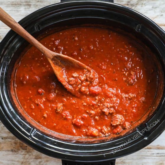 Slow cooker spaghetti sauce with wooden spoon inside pot.