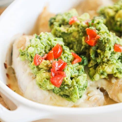 Baked chicken breast in a pan topped with guacamole and tomatoes.