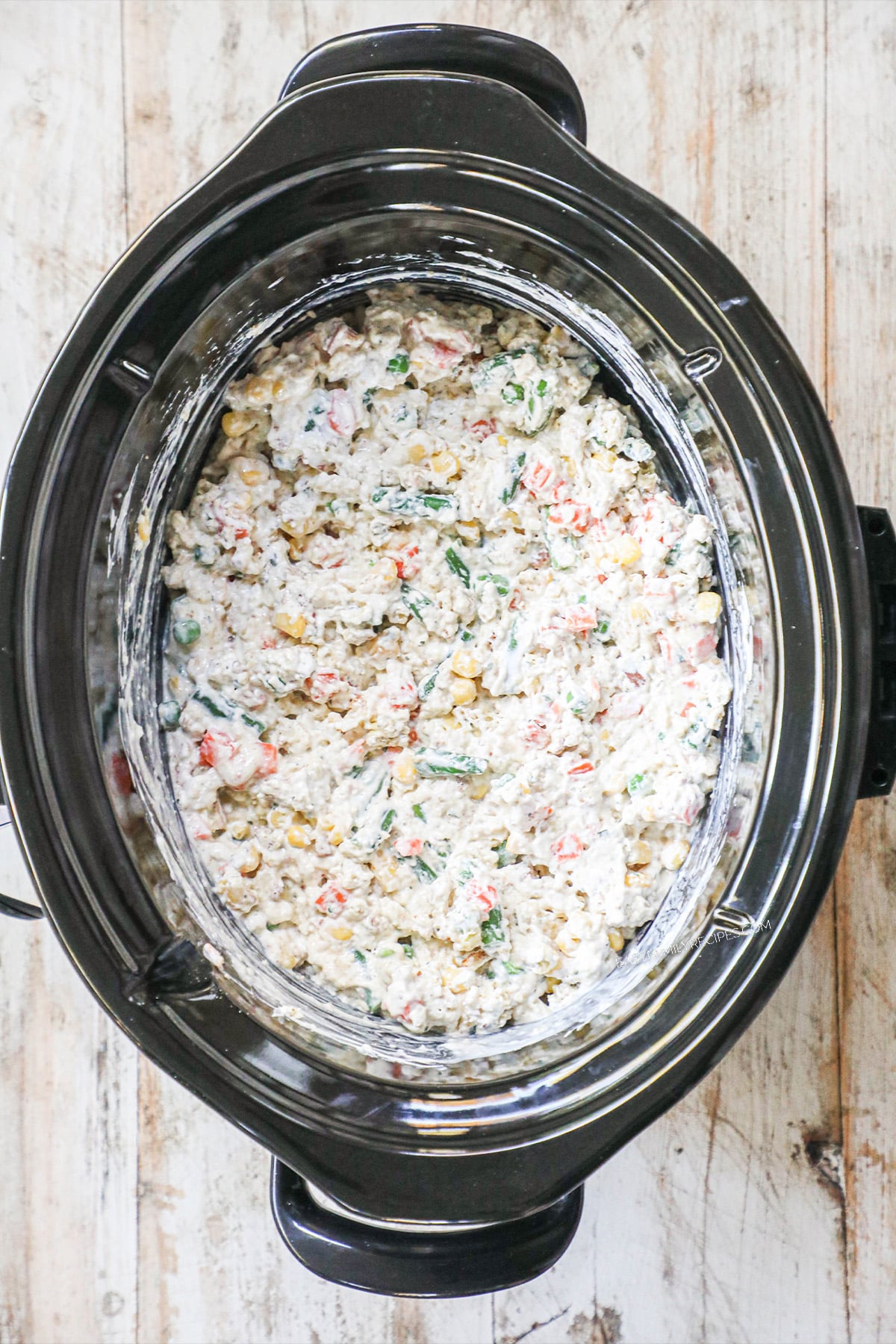 Chicken and stuffing ingredients mixed together in a slow cooker before being cooked.