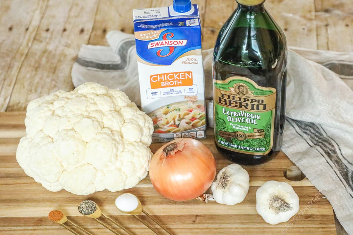 ingredients to make cauliflower soup including cauliflower, chicken broth, olive oil, garlic, onion, and spices.