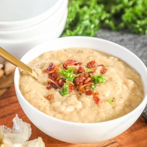 a bowl of cauliflower soup topped with bacon and green onions.
