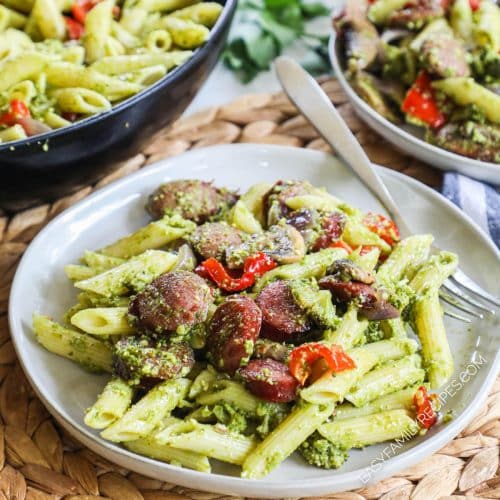 Completed smoked sausage and pesto pasta with veggies on a plate.