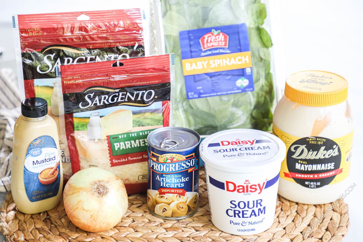 Ingredients for spinach artichoke dip including mozzarella, parmesan, onion, mustard, artichoke hearts, spinach, sour cream, mayo, and alt and pepper.