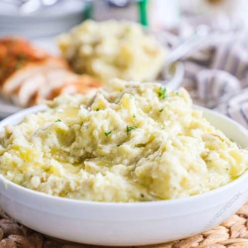 side view of a white bowl piled with cheesy mashed potatoes and garnished with chives.