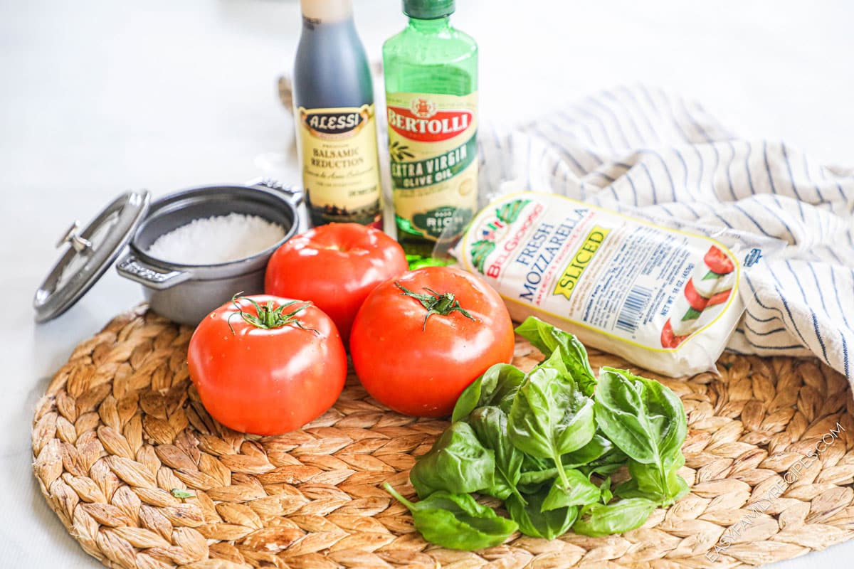 Ingredients for recipe before prepping: salt, tomatoes, mozzarella, balsamic reduction, olive oil, and fresh basil.
