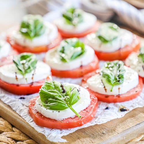 Close up angle of Caprese salad with a whole basil leaf on each slice of tomato and mozzarella and balsamic glaze.