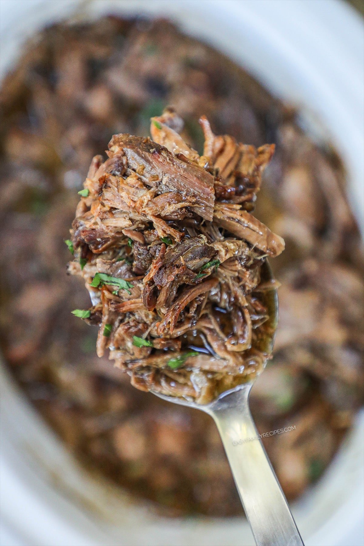 scoop of french onion pot roast being lifted from crockpot on a spoon
