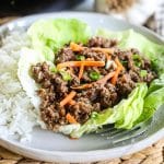Korean beef inside a leaf lettuce cup with shredded carrots and a side of white rice.