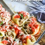 A glass casserole dish full of spinach and sausage stuff shells with cheese on top