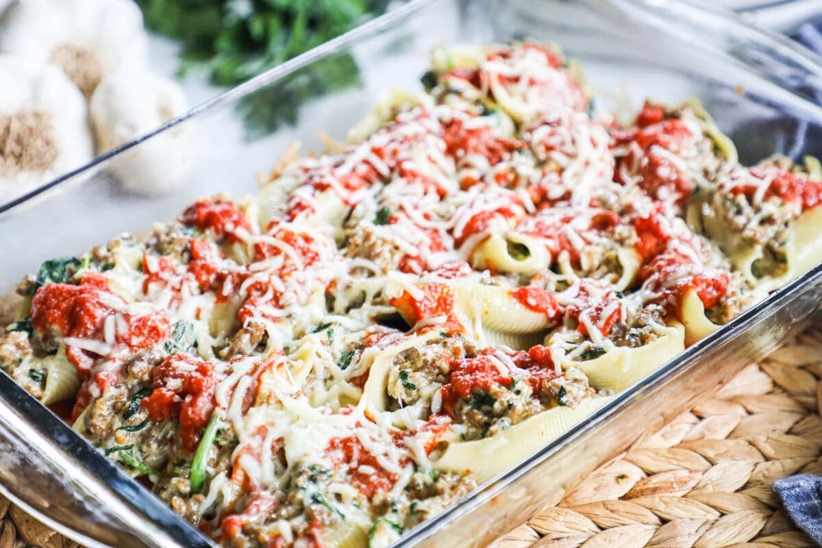 A glass casserole dish full of spinach and sausage stuff shells with cheese on top