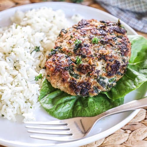A turkey burger with spinach served on a bed of lettuce with rice.