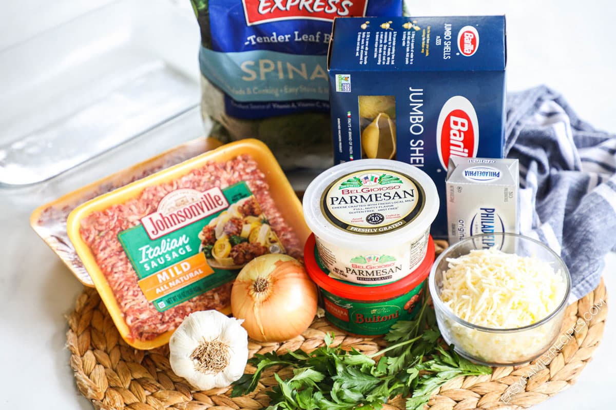 ingredients to make stuffed pasta shells including ground sausage, fresh spinach, cream cheese, onion, garlic, and pasta.