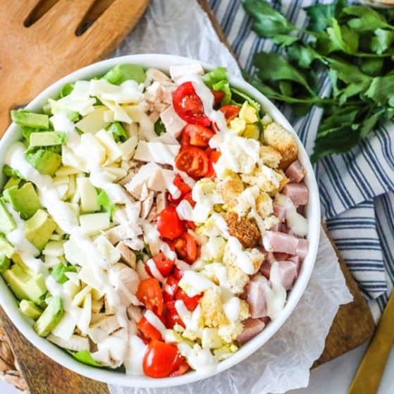Chef salad in a bowl with all ingredients laid out vertically and dressing drizzled over.