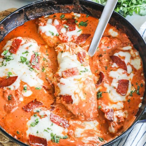 Chicken pizzaiola in skillet with serving spoon lifting piece of chicken