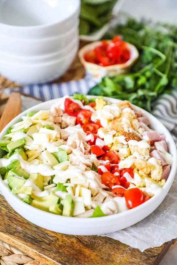 Chef salad in a bowl with all ingredients laid out vertically and dressing drizzled over.