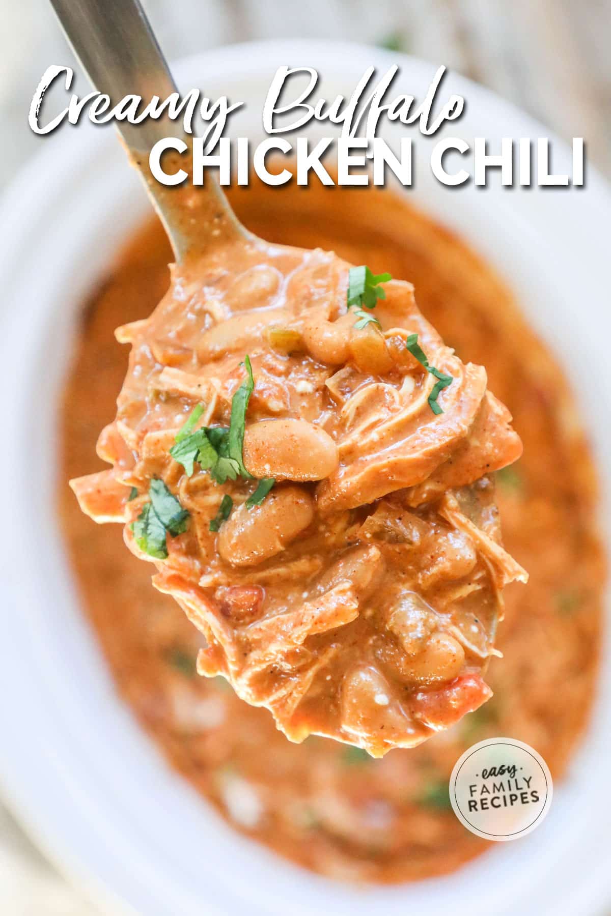 Spoonful of creamy buffalo chicken chili garnished with cilantro, held over crockpot of chili
