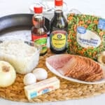 Ingredients for ham fried rice including leftover rice, leftover ham, peas and carrots, onion, eggs, soy sauce, sesame oil, garlic and butter.