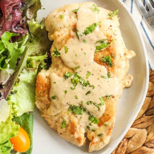 A chicken breast with a honey Dijon sauce served beside salad.