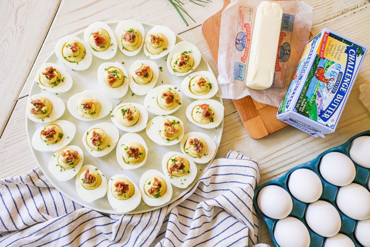 Deviled Eggs with bacon on a platter sitting next to butter and hard boiled eggs