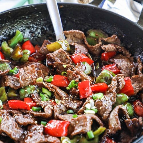 A metal spoon scooping stir fried steak and bell peppers from a large pan.