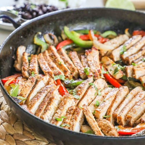 Thinnly sliced pork fajitas with red and green bell peppers in a pan.