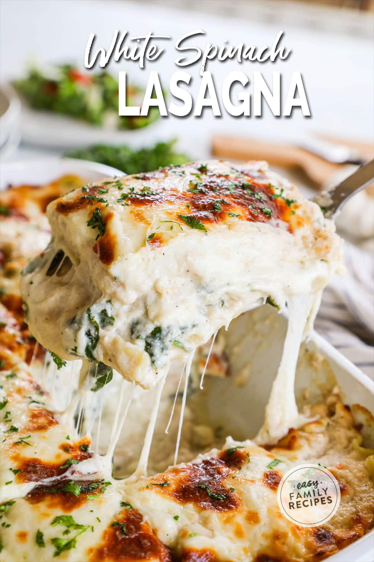 White vegetable lasagna showing layers of noodles, white sauce, and cheese as it is lifted out of a dish