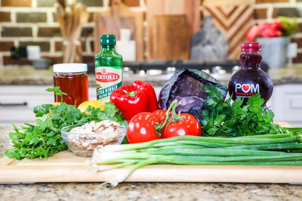 Ingredients for spring chopped salad with pomegranate dressing including cabbage, cilantro, parsley, red pepper, tomato, green onion, and crunchy almonds, and pomegranate juice.