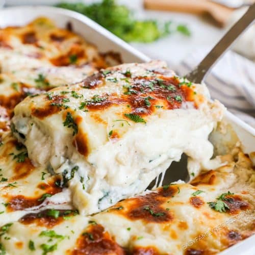Lifting a slice of white spinach lasagna out of the casserole dish