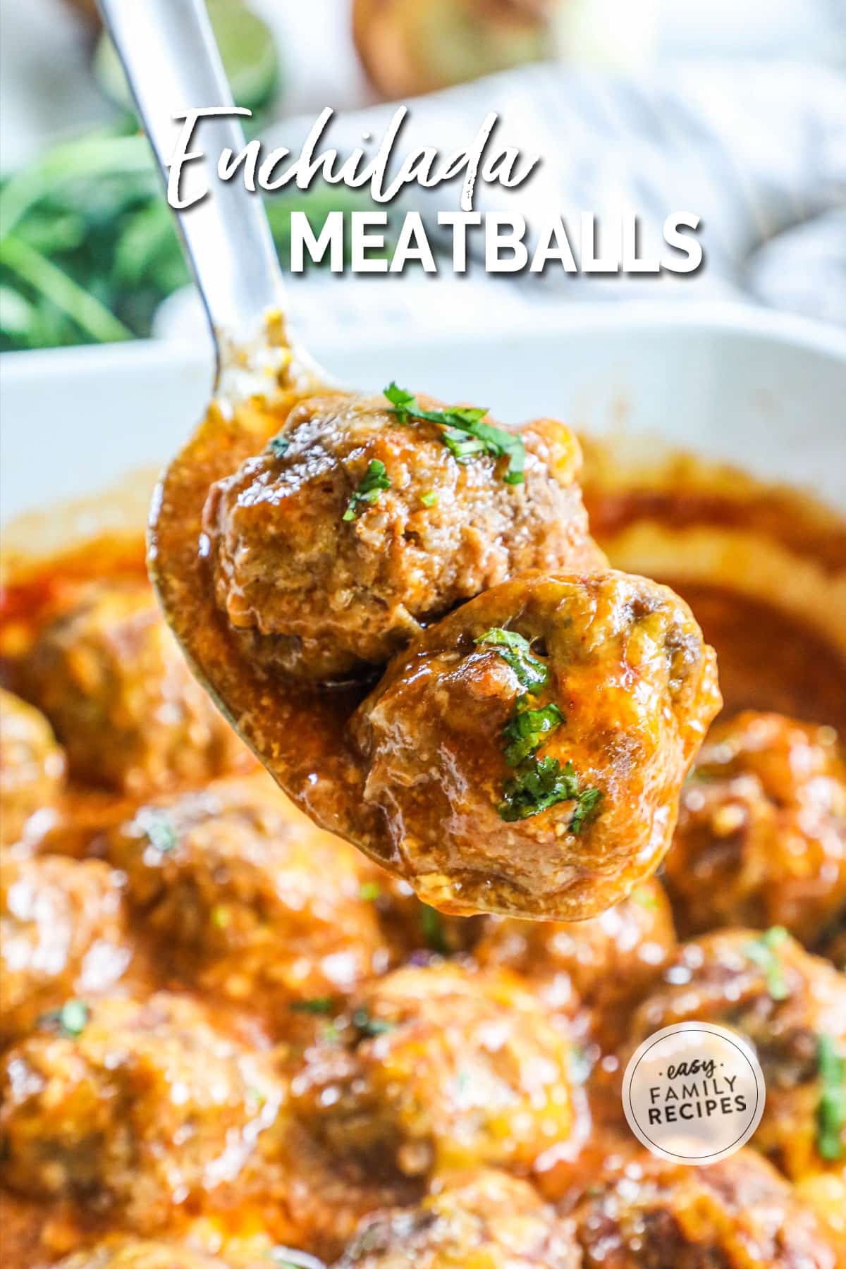 Spoon lifting up two cheesy and saucy enchilada meatballs from a baking dish.