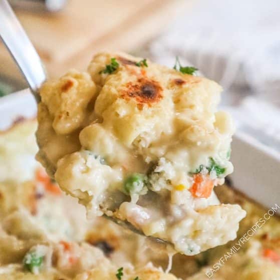 A spoon scooping creamy chicken and vegetable casserole from a pan.
