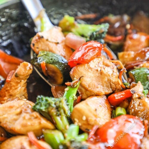 Close up of a spoon scooping up chicken veggie stir fry.